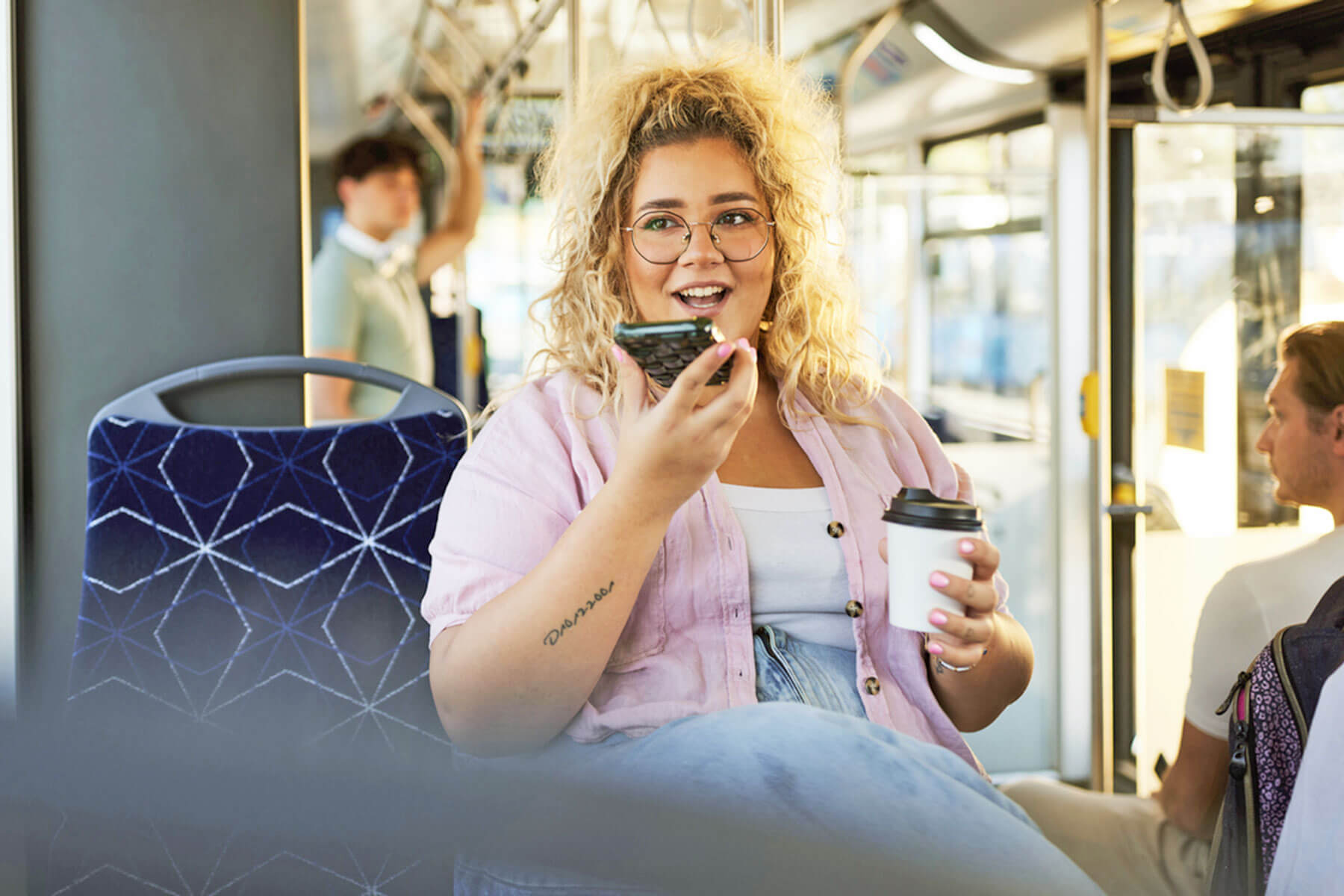 Woman holding a coffee and talking on speakerphone. 