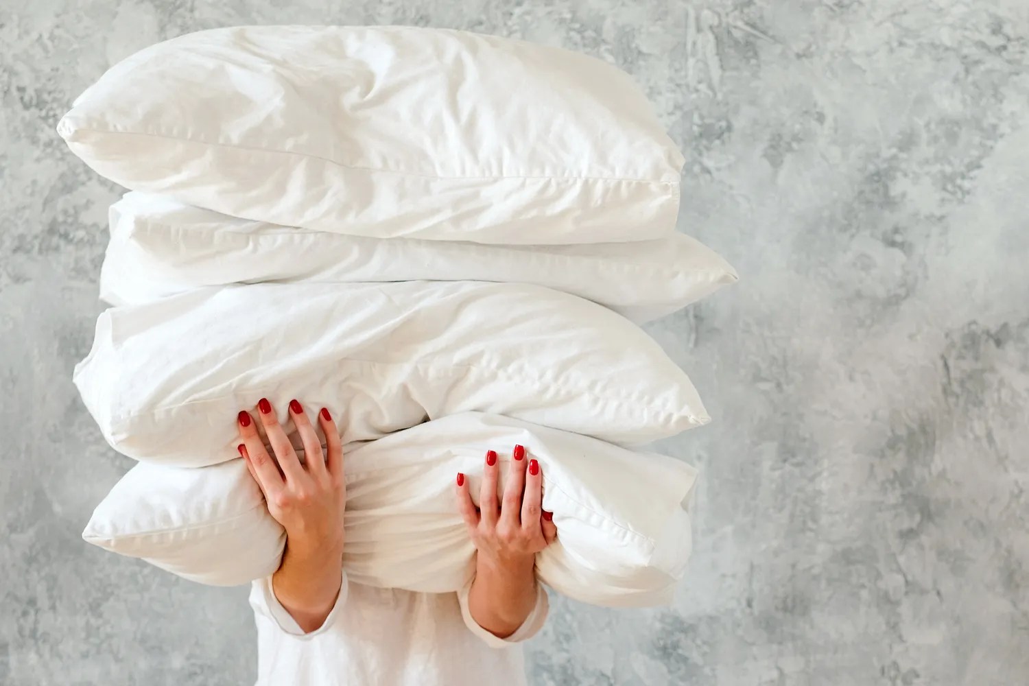 A person holding four pillows, covering their face