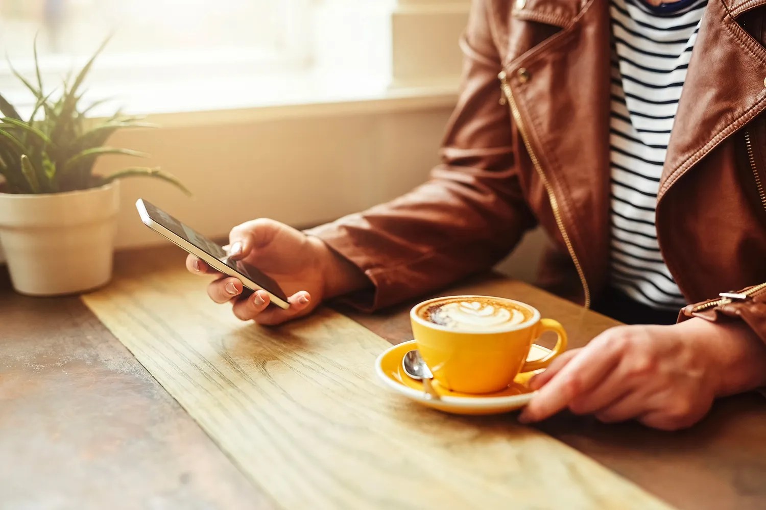 Person sitting at table with a coffee in front of them while looking at their phone. 