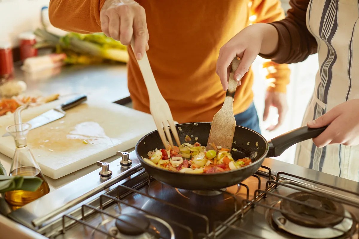Two people preparing a stir-fry in a pan 