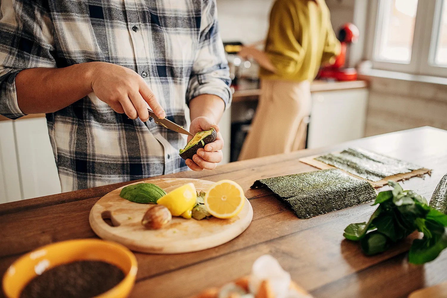 Person slicing an avocado, with lemon and seaweed on a counter 