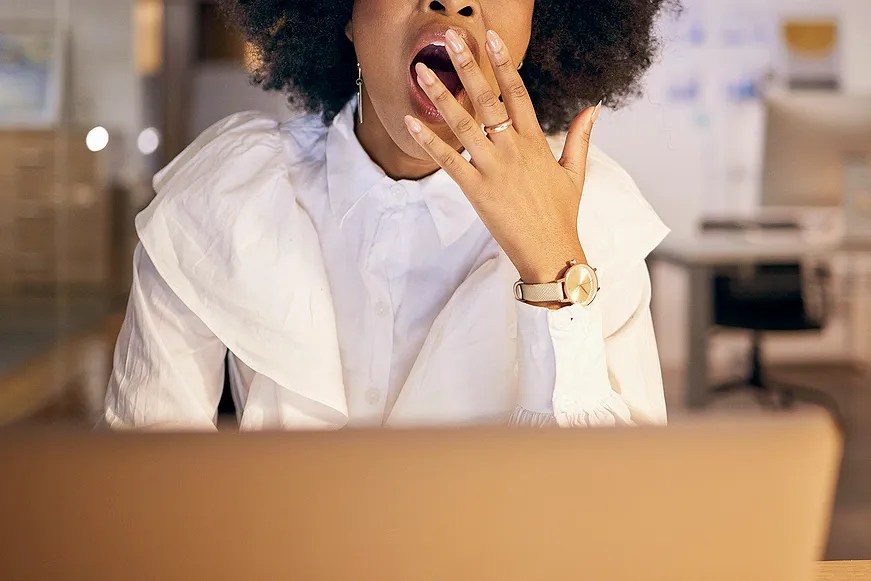 Woman sitting at desk, yawning.