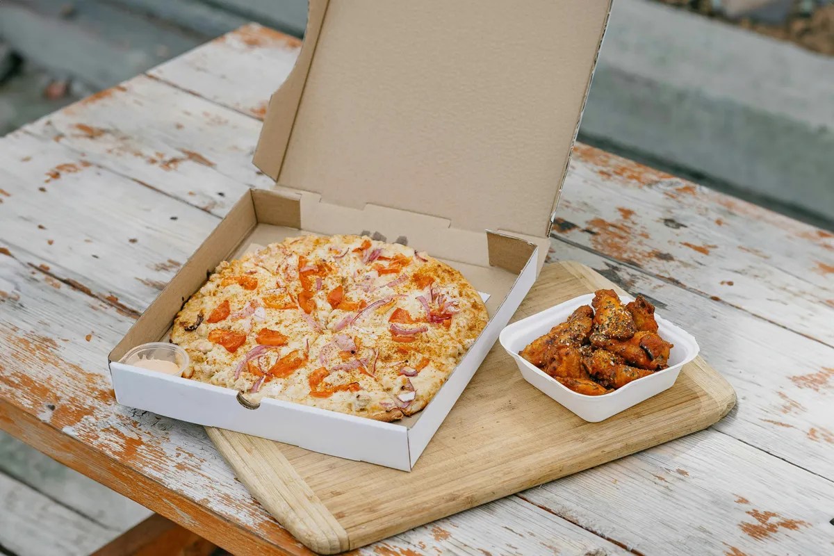 Open box of pizza next to carton of chicken wings. 