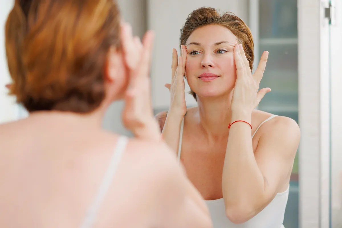 Adult woman massaging face around eyes in front of bathroom mirror  