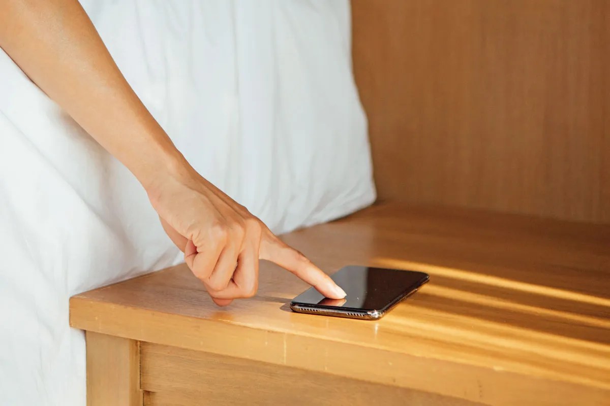 Person pressing their phone screen with their phone on a table. 