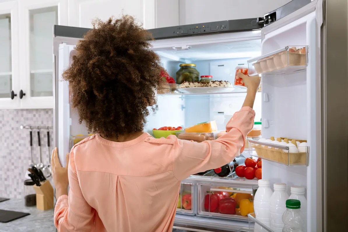 Person looking in fridge and picking up a container of fruit