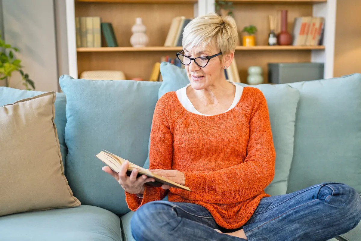 woman reading book at home on couch