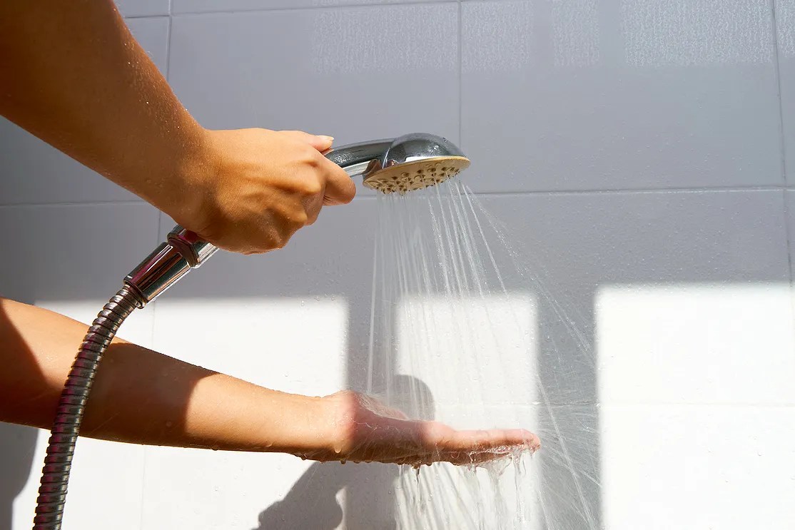 Person running a shower head onto the palm of their hand. 